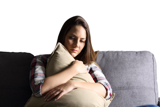 Front view of a sad girl embracing a pillow sitting on a couch